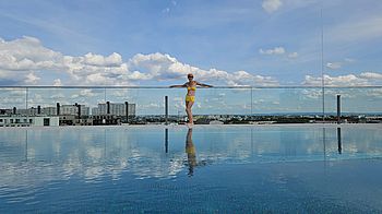 Eine Frau im Bikini steht auf einer Dachterrasse mit Pool, im Hintergrund Wien