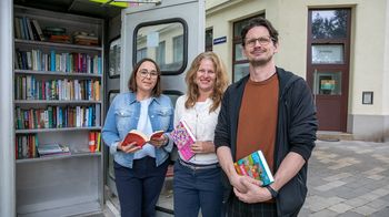 Bücherschrank in alter Telefonzelle. Davor stehen BV-StV Julia Lessacher, Karl Lampret und Annelies Larcher (GB*)
