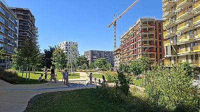 Menschen spielen bei Sonnenschein mit dem Wasserspiel im Bert-Brecht-Park
