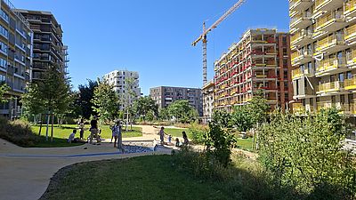 Menschen spielen bei Sonnenschein mit dem Wasserspiel im Bert-Brecht-Park