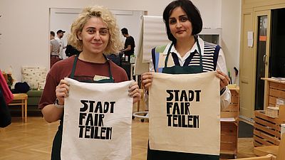 zwei Personen, weiblich gelesen, halten Tasche mit Druck "Stadt fair teilen"