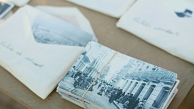 Alte Schwarz-Weiß-Fotos in Stapeln und teilweise in Briefumschlägen auf einem Holztisch sortiert.