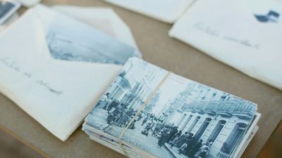 Alte Schwarz-Weiß-Fotos in Stapeln und teilweise in Briefumschlägen auf einem Holztisch sortiert.