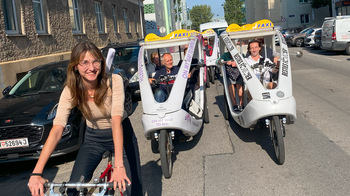 Personen fahren mit Fahrrad oder im Fahrradtaxi auf der Straße.