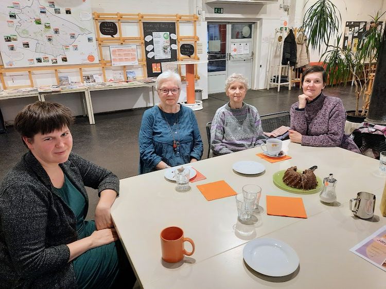 Vier Damen an einem gedeckten Tisch schauen in die Kamera.