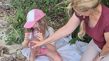 Zwei Personen erforschen mit Becherlupen Wald und Hecke.