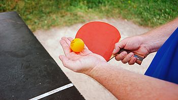 Eine Person hält einen Tischtennisschläger und einen Ball in den Händen.