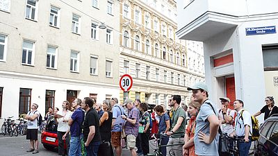 Eine Gruppe Menschen schaut auf ein saniertes Wohnhaus.