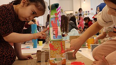 Zwei Kinder sitzen am boden und basteln mit Karton und Farbe.