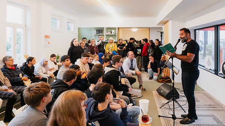 Mann liest vor vielen Kindern und Erwachsenen aus einem Buch vor.