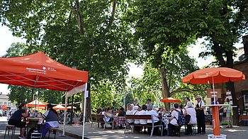 Parksetting mit organgenen Schirmen und Pavillion, Bäume, zahlreiche Personen