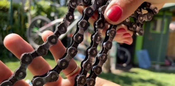 Frauenhände mit roten Nägeln halten eine Fahrradkette 