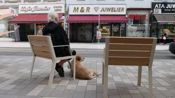 Eine Frau sitzt auf einem Sessel am Gehsteig, daneben ein Hund