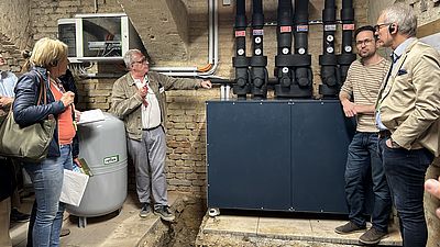Personen stehen bei einer Heizungsanlage im Keller eines saniertes Hauses.