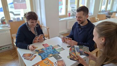 3 junge Menschen spielen das Brettspiel Dixit an einem Tisch.