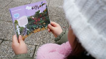 Ein Kind mit einer rosa Jacke und einer weißen Haube liest ein Infobuch