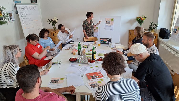 9 Personen sitzen um einen Tisch und beraten über die eingereichten Ideen beim Nachbarschatz Floridsdorf.