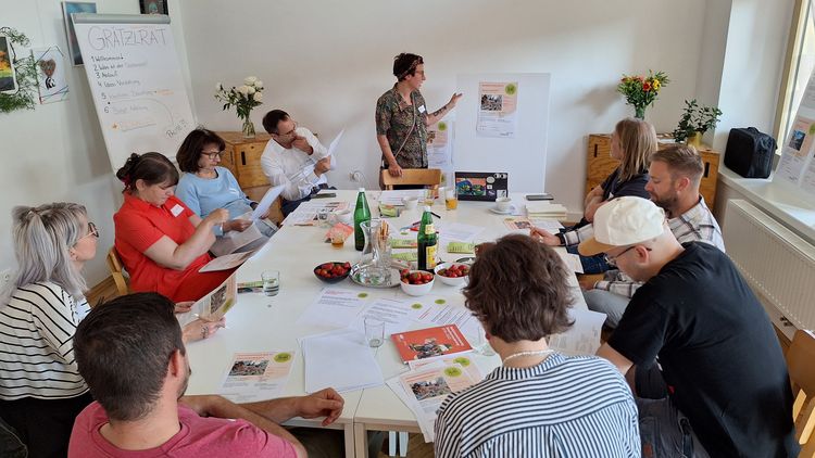 9 Personen sitzen um einen Tisch und beraten über die eingereichten Ideen beim Nachbarschatz Floridsdorf.