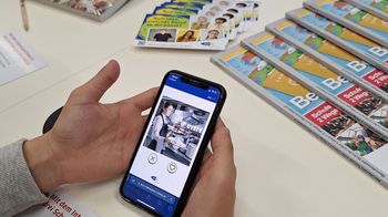 Hände halten Handy mit Film, Infomaterial von AMS liegt am Tisch zu Green Jobs