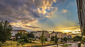 Sonnenuntergang hinter Wohnhäsern, im linken Vorderdrung ist ein Park mit Laubbäumen.