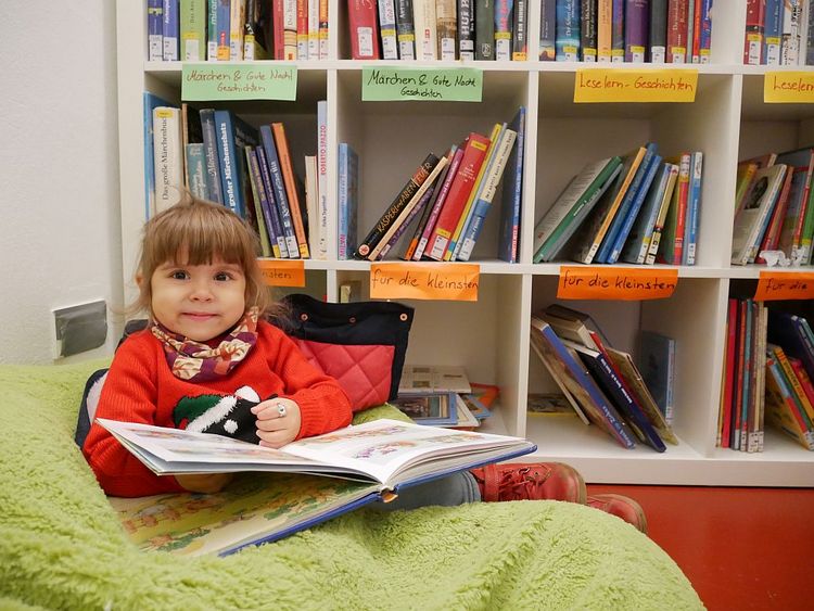 In der Minibücherei. Ein kleines Mädchen sieht sich ein Buch an.