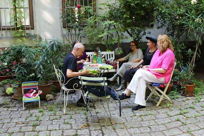 4 Personen sitzen auf Gartenstühlen in einem begrünten Innenhof
