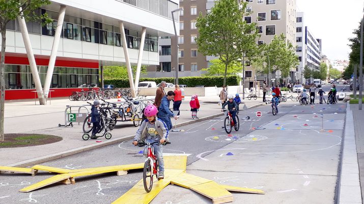Radspielplatz in der Ernst-Melchior-Gasse In einer Fußgängerzone ist ein Radparcours aus gelben Holzplanken aufgebaut, KInder fahren mit Fahrrädern darüber