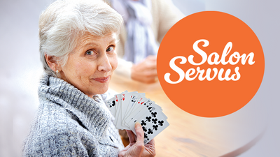 Alte Dame, die französische Spielkarten in der Hand hält und runder Sticker mit Hinweis auf Salon Servus.