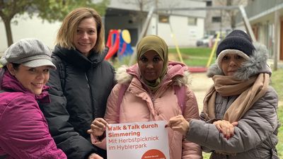 Vier Spaziergängerinnen halten warm eingepackt das Veranstaltungsplakat in die Kamera.