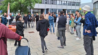 Im öffentlichen Raum steht eine Gruppe von Menschen im Kreis.