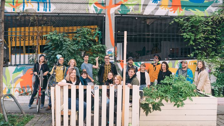Nutzer*innen Garage Grande Eine Gruppe an Menschen vor einer Hochgarage, die mit Kletterpflanzen bewachsen und bunt bemalt ist