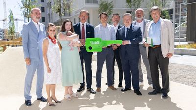 Stakeholder*innen des Baus und der Entwicklung des VILLAGE IM DRITTEN halten einen übergroßen, grellgrünen Schlüssel in die Kamera, mit Ihnen neue Bewohner*innen: eine Jungfamilie mit Baby.