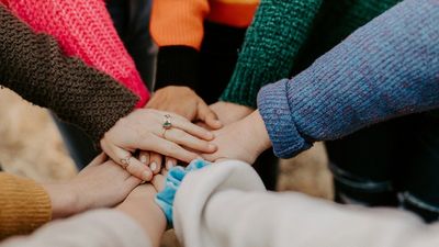 mehrere weiße Hände übereinander, bunte Pullover
