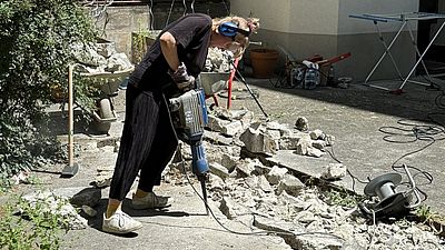 Frau und Bohrer beim Aufbrechen einer Asphaltfläche