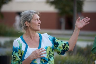 Eine Frau mit weiß-blau-grüner Bluse gestikuliert mit den Händen