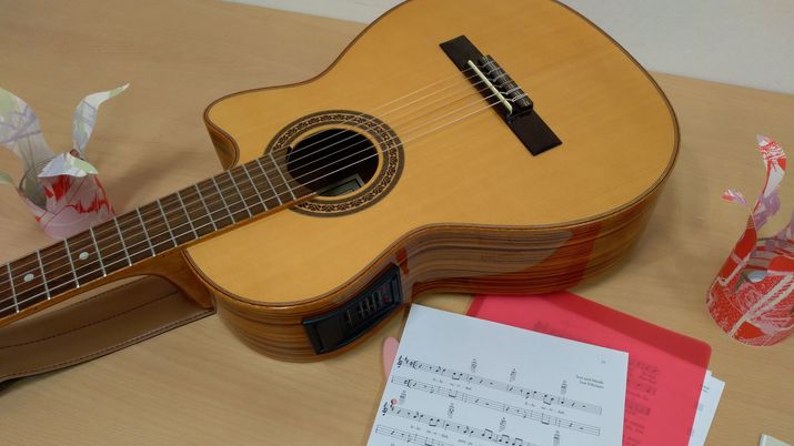 Auf einem Tisch liegt eine Gitarre, daneben Notenblätter