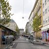 Blick in eine Straße mit bunten Hausfassaden, links und rechts neu gepflanzte Bäume mit grünen Blättern