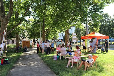 Park mit Liegestühlen und Pavillion, mehrere Persone sitzend und stehend, sonnig, grün