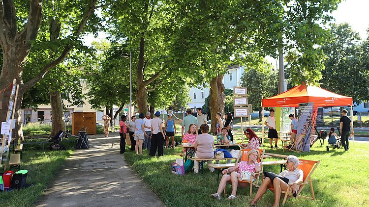 Park mit Liegestühlen und Pavillion, mehrere Persone sitzend und stehend, sonnig, grün