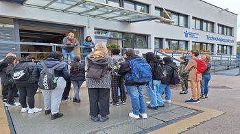 Gruppe von jungen Personen steht vor Gebäude mit Aufschrift Jugend am Werk. Zwei erwachsene Personen stehen oben und erzählen