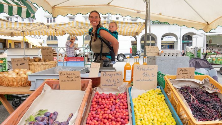 Marktstandlerin vom Bauernmarkt hinter ihrem Stand, Kind am Rücken