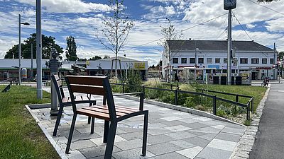 Zwei Stühle draußen, Trinkwasserbrunnen, Grasfläche und Sträucher