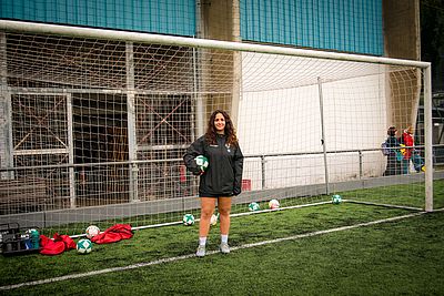 Die Trainerin Mana-Marielle steht vor einem Fußballtor und hält einen Ball in der Hand.