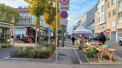 Herbstlich verfärbte Bäume und Marktstände auf einem Platz, Sonnenschein und blauer Himmel