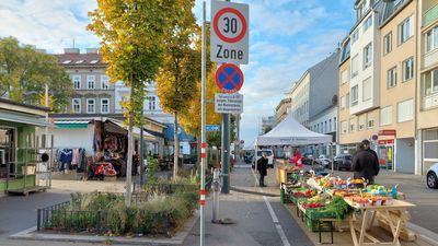 Herbstlich verfärbte Bäume und Marktstände auf einem Platz, Sonnenschein und blauer Himmel