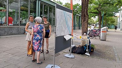 Drei Personen stehen neben einer Pinnwand und unterhalten sich.