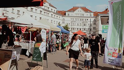Markt mit vielen Ständen, Menschen laufen herum. im Hintergrund weiße Häuser