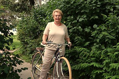Herta mit dem Fahrrad zwischen grünen Büschen.