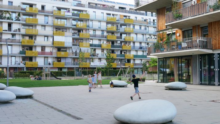 Kinder spielen auf einem Platz, dahinter zwei neue Wohngebäude