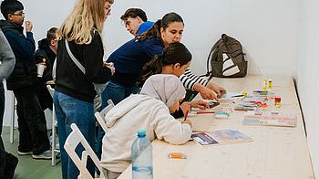 Kinder sitzen an Tisch und basteln.